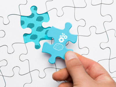 close-up-human-hand-holding-blue-puzzle-piece-with-brain-cogwheel-drawing